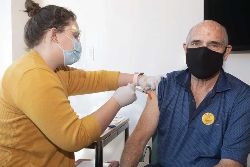 a health care worker administering a vaccine in the upper arm to an elderly person